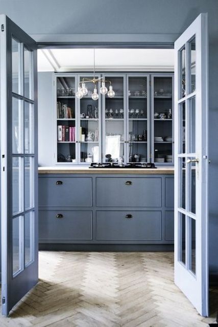 an ocean blue kitchen with flat panel and glass front cabinets, a stone countertop, built-in appliances and a cool chandelier