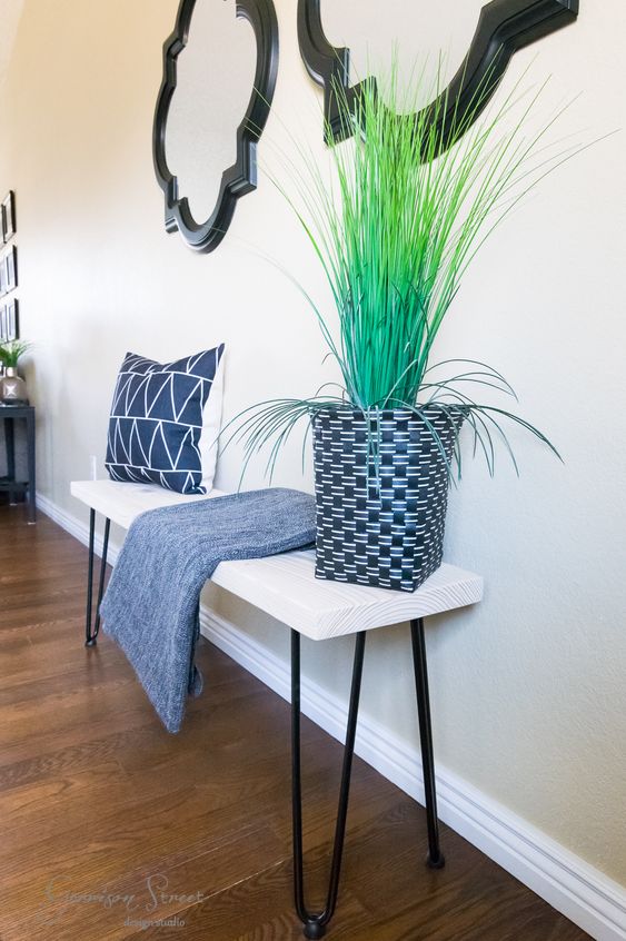 a whitewashed bench with black hairpin legs, a potted plant, a printed pillow and a blanket for a cozy entryway
