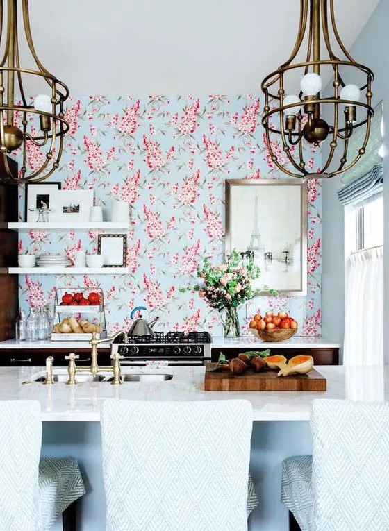 a bright and catchy space with only lower cabinets, with bright floral wallpaper, open shelving,a kitchen island with seating and large chandeliers