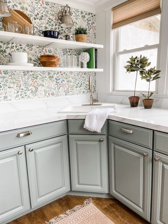 a grey farmhouse kitchen with white stone countertops, a floral wallpaper wall, open shelves and potted plants plus brushed sconces