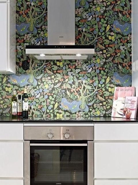 a minimalist black and white kitchen spruced up with a dark floral wallpaper backsplash is a stylisha dn cool space to cook in