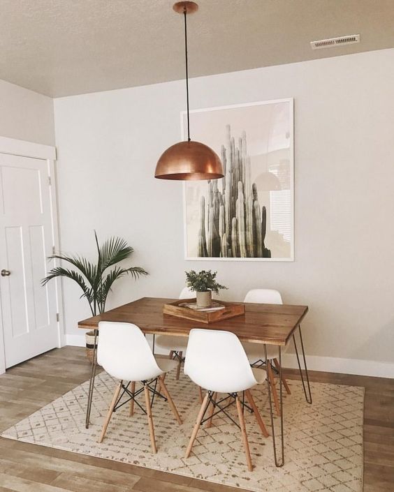 a boho desert dining space with a hairpin leg table, white chairs, a boho printed rug, an artwork, potted greenery and a copper pendant lamp