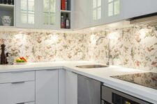 12 a small white kitchen with flat panel cabinets, a floral wallpaper backsplash and glass front cabinets plus sleek stone countertops