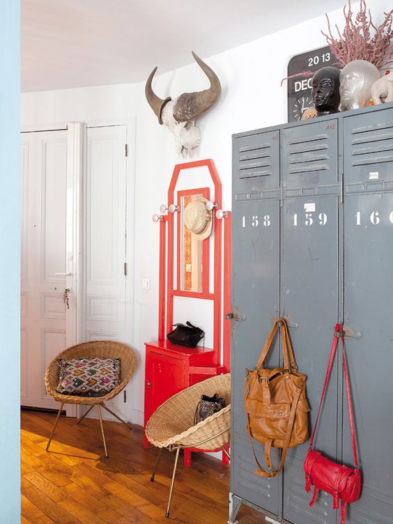 an eclectic space with grey metal lockers, a bold red console table, rattan chairs, bold bags and bright decor on top the lockers