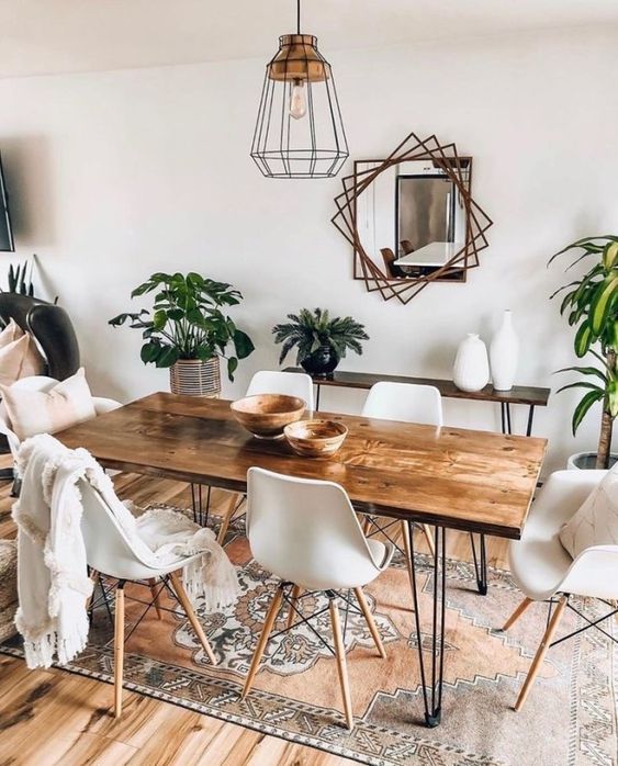 a boho dining room with a hairpin leg dining table, white chairs, a hairpin console table, potted greenery, a mirror with a catchy frame