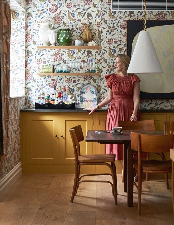 a vintage yellow kitchen with black countertops, open shelving and bright floral wallpaper plus a chic and elegant dining zone