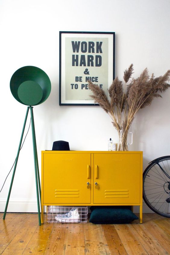 a mid-century modern entryway with a mustard locker, pampas grass, a green floor lamp and a metal basket for storage
