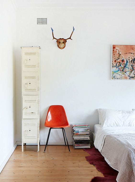 an airy mid-century modern bedroom with a low bed, neutral bedding, an orange chair, a stack of books and ivory lockers for storage