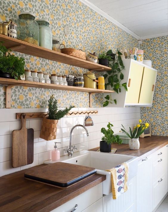 a bold cottage kitchen with white beadboard cabinets, colorful floral wallpaper, open shelving, a small yellow cabinet and butcherblock countertops