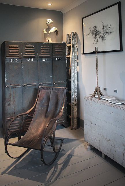 an industrial space with shabby chic black metal lockers, a leather rocker chair, an artwork and a folding shabby chic table