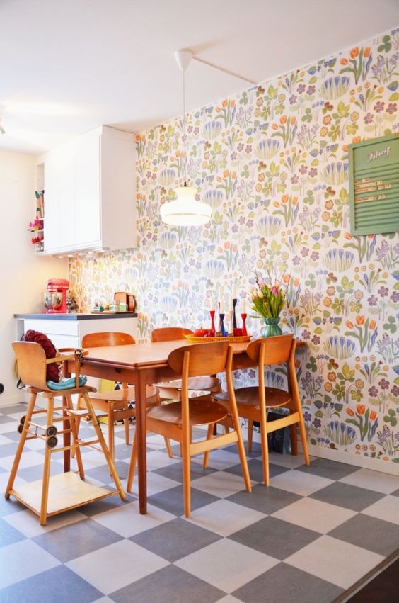 a bright retro eat-in kitchen with a colorful floral wallpaper wall, white furniture and stained dining furniture, a checked floor is cozy and cool