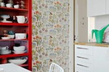 23 a catchy kitchen with white flat panel cabinets, a red buffet with dishes and bright floral wallpaper, a white dining set