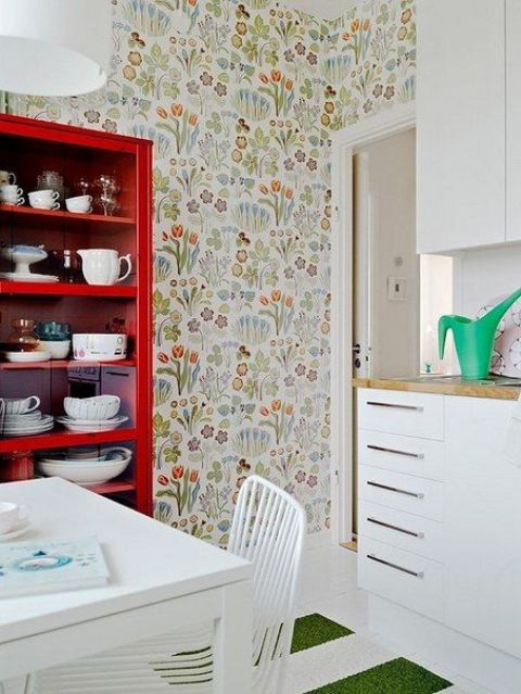 a catchy kitchen with white flat panel cabinets, a red buffet with dishes and bright floral wallpaper, a white dining set