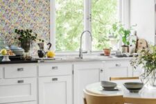 24 a chic cottage kitchen with white shaker cabinets, a bright floral wallpaper wall, stone countertops and black pendant lamps