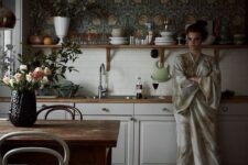 25 a chic creamy kitchen with shaker cabinets, butcherblock countertops, an open shelf and dark floral wallpaper plus some decor