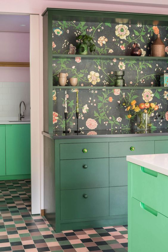 a dark green kitchen with a bold green kitchen island, dark floral wallpaper in the back of a buffet and beautiful decor