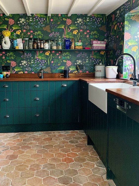 a dark green kitchen with bright floral wallpaper, an open shelf and butcherblock countertops, a hexagon tile floor