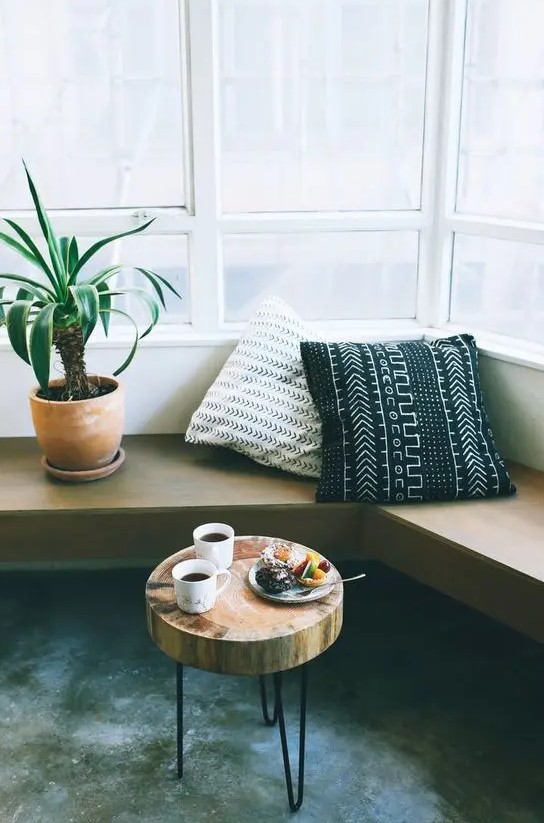 a mid-century modern corner space with a wall-mounted bench with printed pillows, a tree slice side table on hairpin legs is cool
