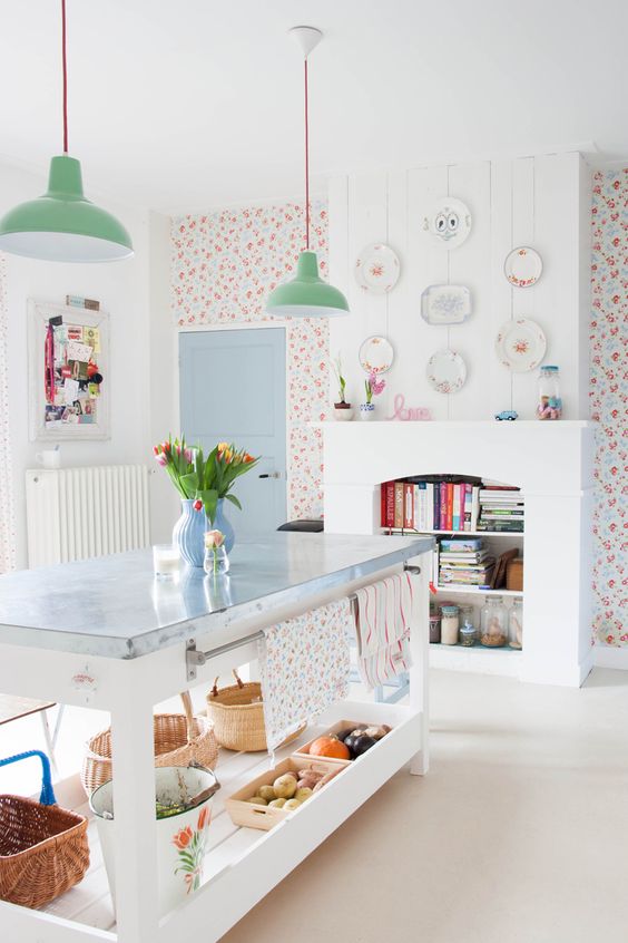a kitchen with bright floral wallpaper, a non-working fireplace with book storage, a kitchen island and green pendant lamps