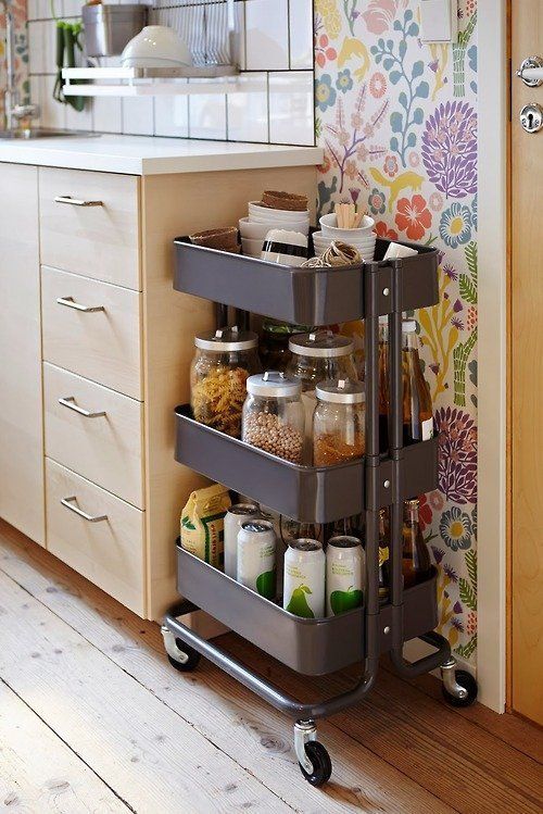 a neutral kitchen with a bright floral wallpaper wall, a dark trolley and a white square tile backsplash is a stylish space