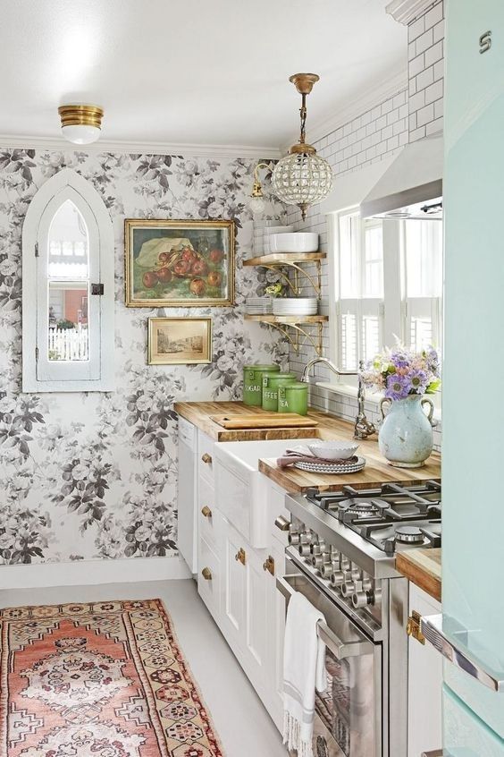 a vintage kitchen with white shaker cabinets, a black and white floral wallpaper wall, butcherblock countertops, open shelves and a subway tile backsplash