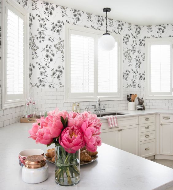 a white farmhouse kitchen with only lower cabinets, white stone countertops, a white subway tile backsplash and floral wallpaper