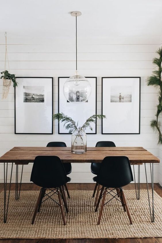 a Scandinavian dining room with a hairpin leg dining table, stylish black chairs, a gallery wall and some greenery around