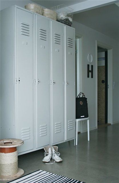 a neutral Scandinavian entryway with metal lockers, a white stool, a printed rug and some baskets and a metal piece on top is amazing