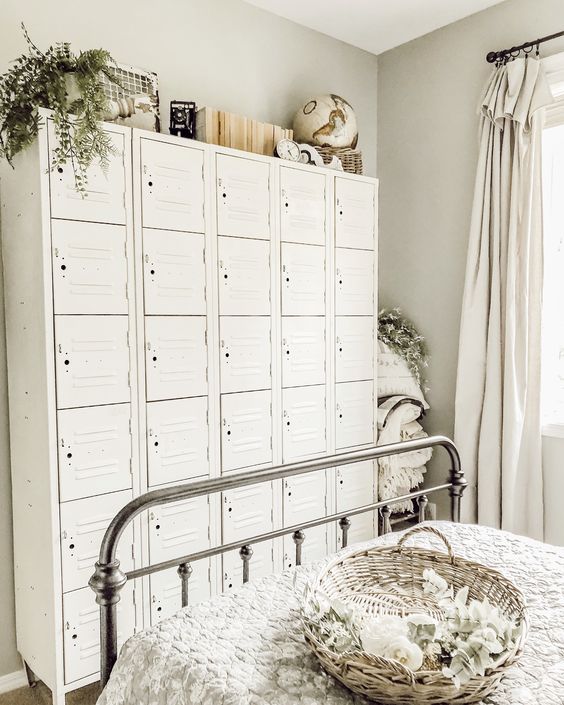 a farmhouse Scandi bedroom with a metal bed, neutral bedding, a stack of white lockers, potted greenery and some decor on top