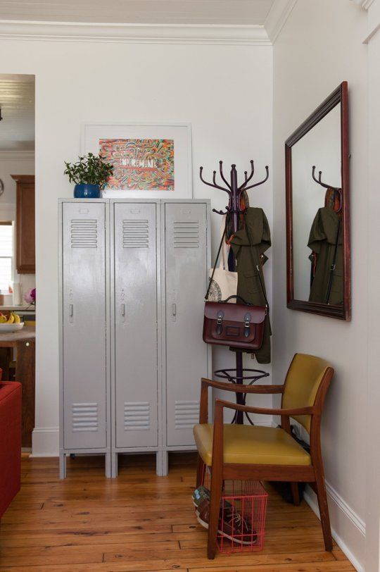 a mid-century modern mudroom with grey lockers, a mustard chair, a mirror in a dark-stained frame, a rack and some bright decor