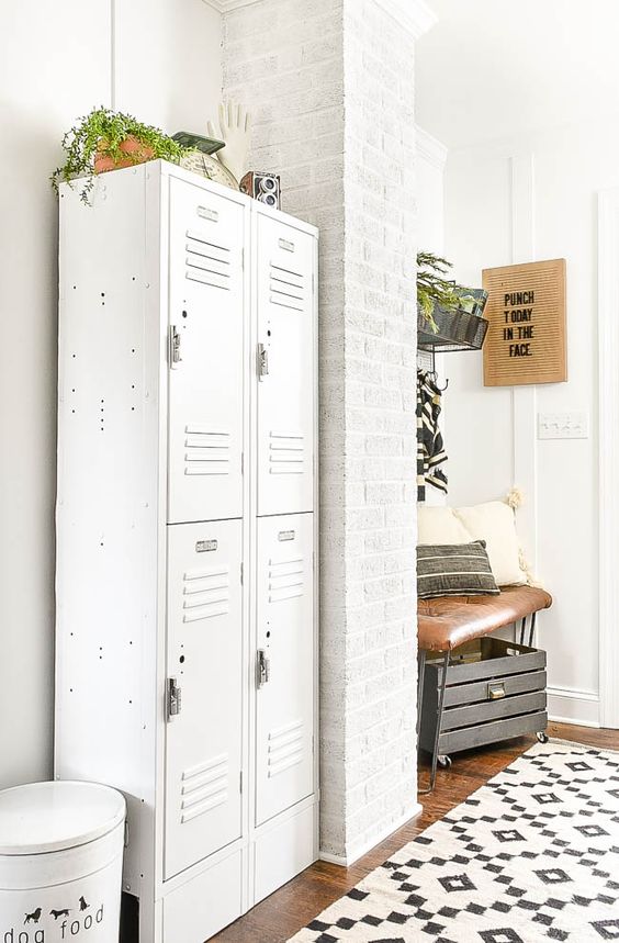 a modern farmhouse murdroom with brick walls, white lockers, a leather upholstered bench, a crate and a printed rug