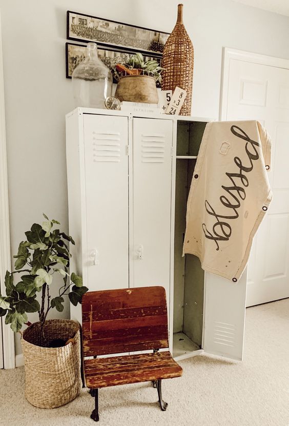 a neutral farmhouse space with creamy lockers, a shabby chic chair, artwork, potted greeneyr and a woven lamp