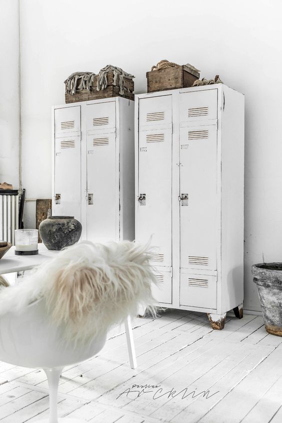 a white Scandinavian space with white lockers, a white table and a chair, some wooden crates for storage is a cool room