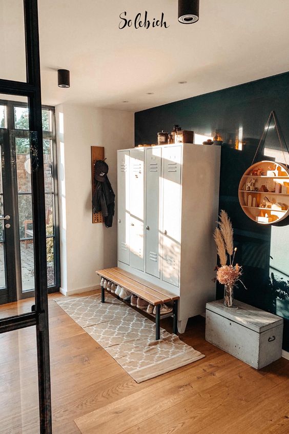 a stylish farmhouse entryway with white lockers, a wooden bench and a chest, a black accent wall and a suspended round shelving unit