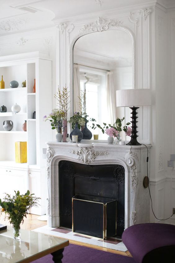 a French fireplace with a gorgeous mantel, a built-in mirror with frame as part of molding, a black screen a a built-in bookcase next to it
