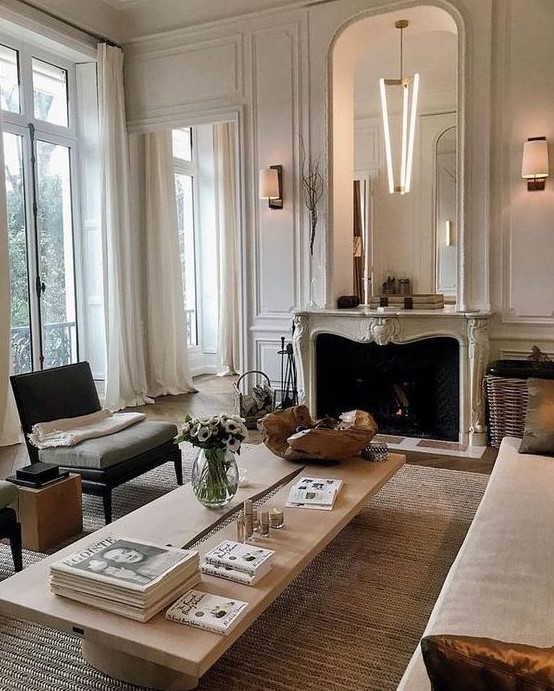 a French style living room done in neutrals, stylish seating furniture, a low coffee table, a French fireplace and an oversized mirror
