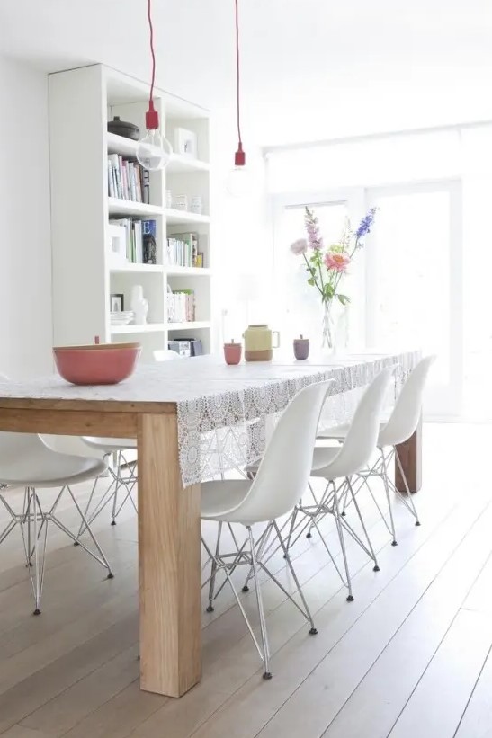 a Nordic dining room with a white bookcase, a light-stained wooden dining table, white Eames chairs and pendant bulbs over the space