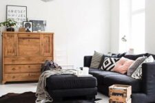 a Nordic living room with a black sofa and a large ottoman, a stained bureau, a crate on casters and potted plants