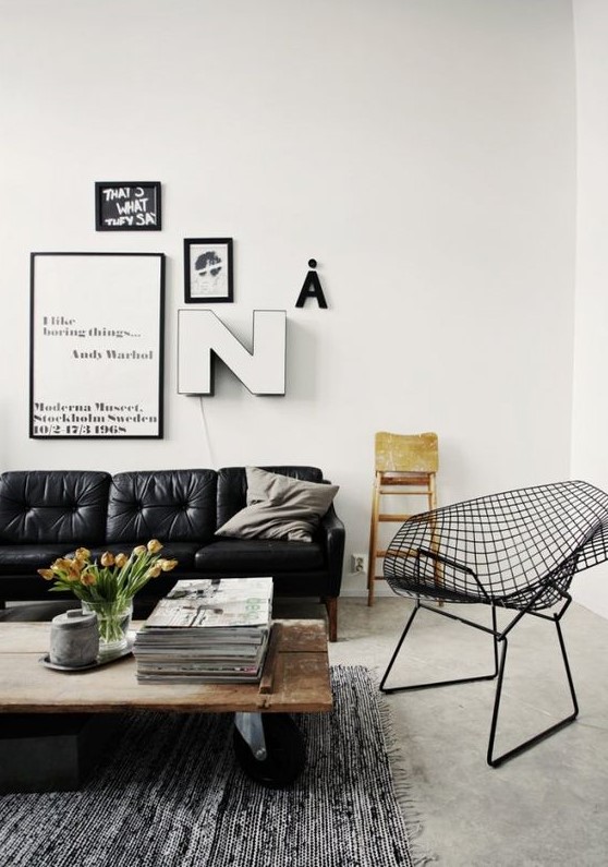 a Scandinavian living room with a black leather sofa, a wooden table on casters and a metal wire chair