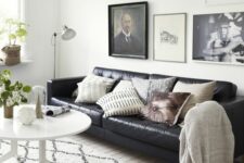 a Scandinavian living room with a black leather sofa, printed pillows, a gallery wall, a white coffee table and potted plants