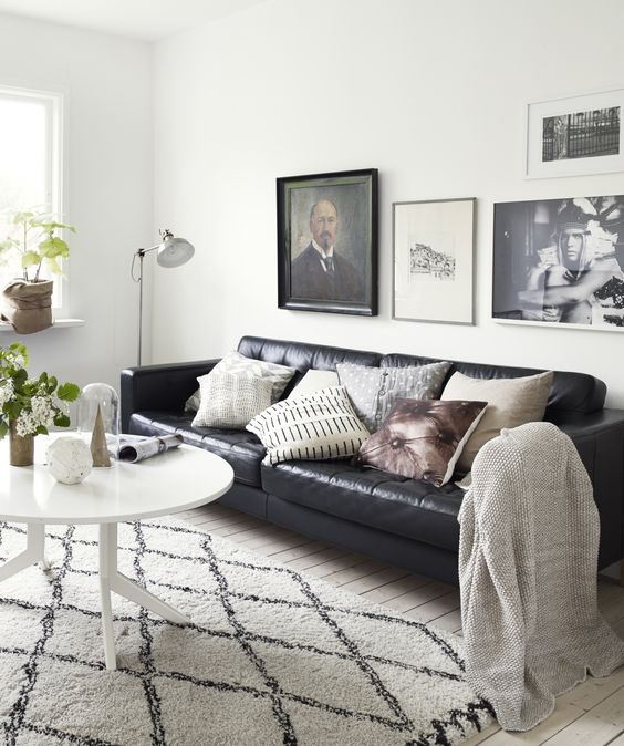 a Scandinavian living room with a black leather sofa, printed pillows, a gallery wall, a white coffee table and potted plants