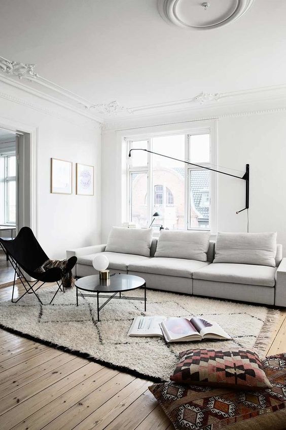 a Scandinavian living room with a large sofa, a black leather butterfly chair, a black coffee table, a black sconce
