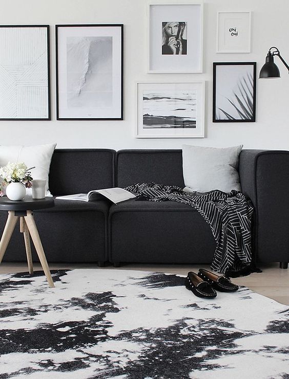 a Scandinavian living room with a low black sofa, a black and white gallery wall, a printed rug and a black floor lamp