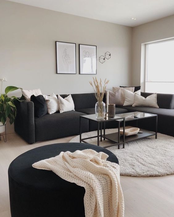 a Scandinavian living room with grey walls, a black sectional, a tiered coffee table, a blakc pouf and a potted plant