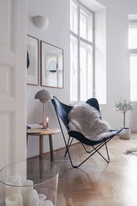 a Scandinavian space with a black leather butterfly chair, a side table with a cool lamp, a mini gallery wall and a glass with candles