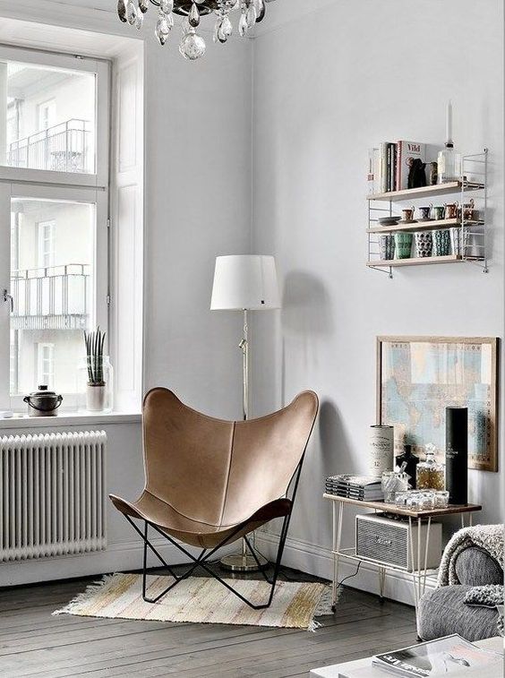 a Scandinavian space with a brown leather butterfly chair, a hairpin leg table, a shelving unit, a map in a frame and a rug