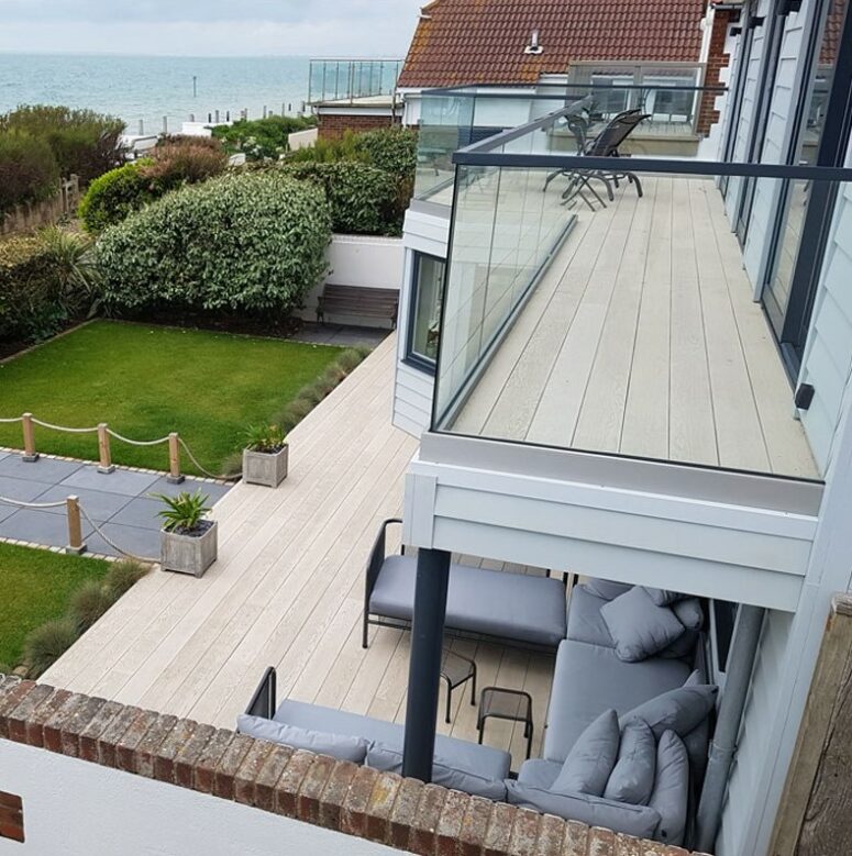 a balcony and a terrace clad with smoked oak decking, with grey upholstered furniture and potted greenery plus a sea view