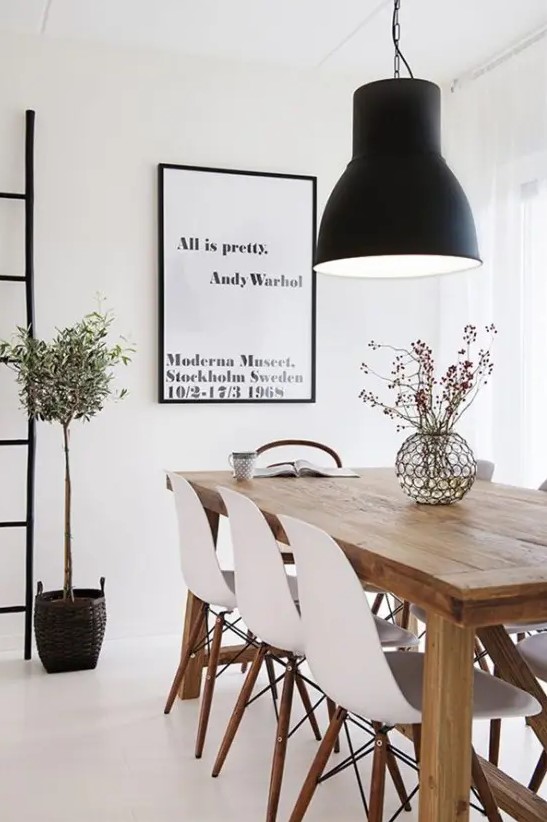 a beautiful Scandinavian dining room with a light-stained wooden table, white Eames chairs, a statement black pendant lamp and an artwork