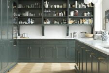 a beautiful dark green English-inspired kitchen with shaker and open cabinets, white countertops and a backsplash, brass and gold fixtures