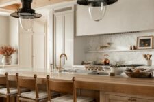 a beautiful earthy kitchen with white cabinets and a built-in hood, a large stained kitchen island, vintage pendant laps